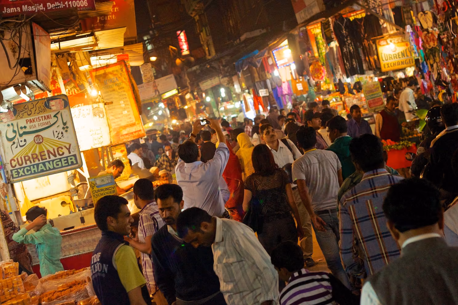 Busy street scene with pedestrians, rickshaws, and shopfronts in the narrow lanes near Jama Masjid, Old Delhi.