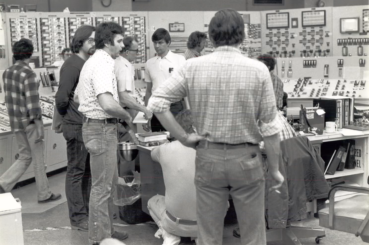 Black-and-white photo of operators crowded around banks of analog dials and indicator panels in the Three Mile Island Unit 2 control room during the 1979 crisis.